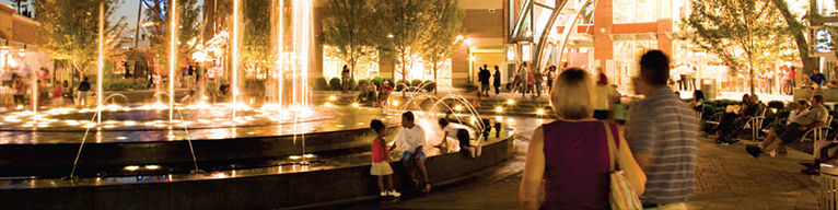 A brightly lit fountain surrounded by people and trees.